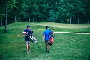 Two men walking across a golf course carrying their bags.