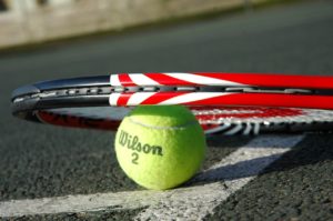 A tennis racket lying on top of a tennis ball on the court.
