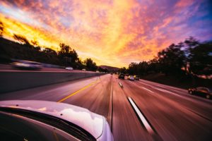 A car driving along an expressway at sunset.