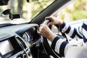 Person wearing a blue and white striped shirt with their hands on the wheel of a car.