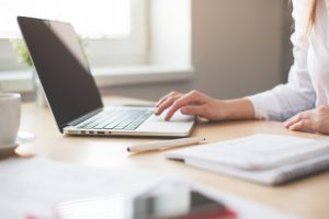 A woman sitting at a wooden desk browsing the Internet on her laptop.