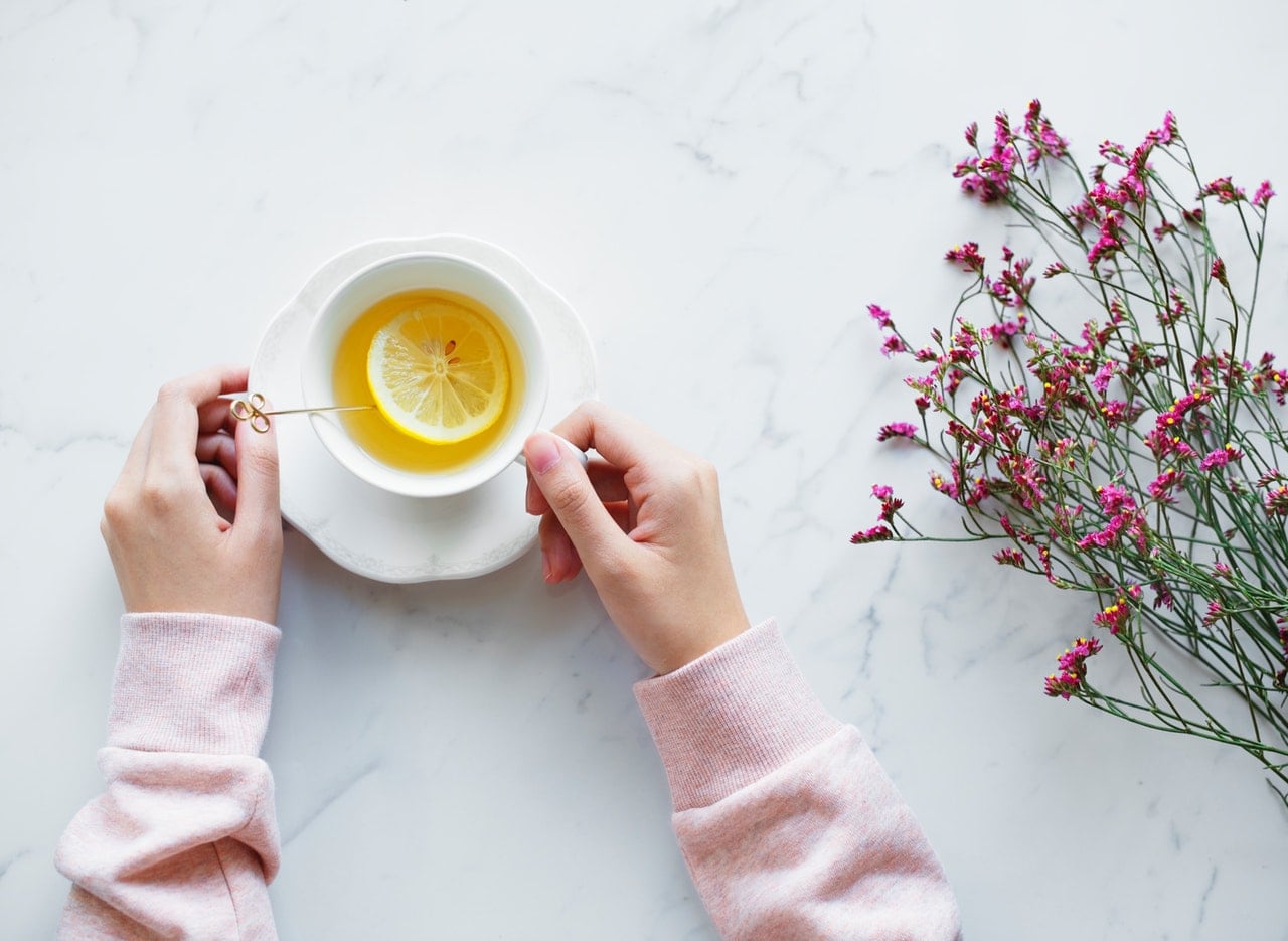 A woman holding a tea cup with hot tea in it, adding a lemon.