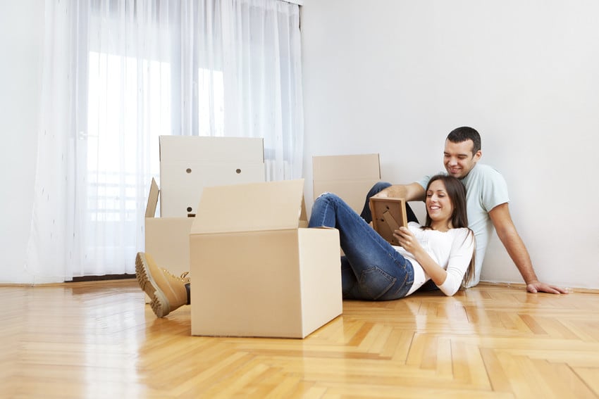 A couple sitting down in their new home, surrounded by unpacked boxes.