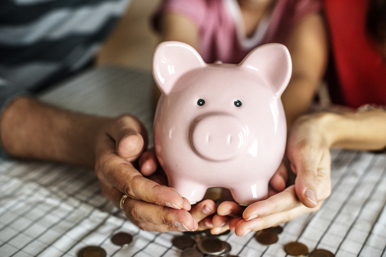 Three family members holding a pink piggy bank that is spilling out coins.
