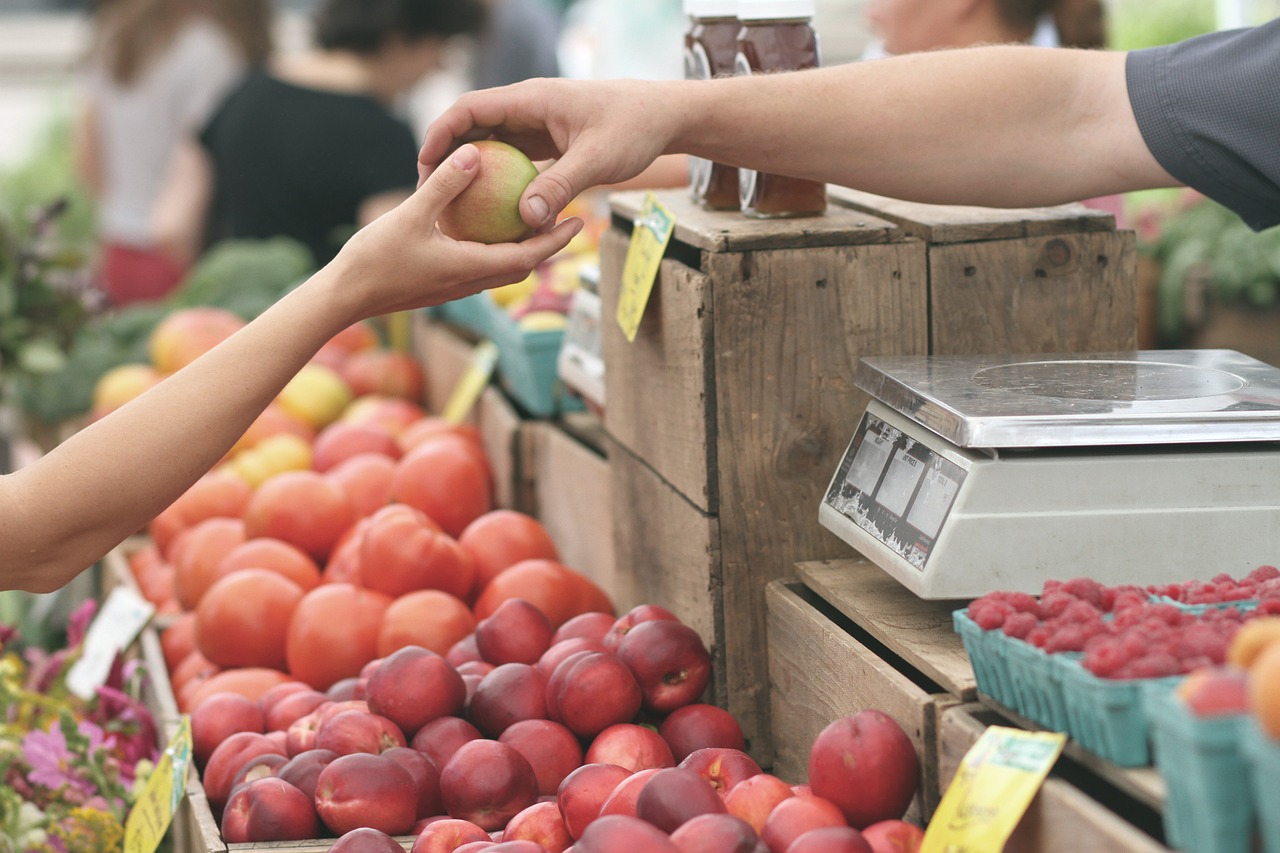 A woman reaching for peaches at the farmer's market.
