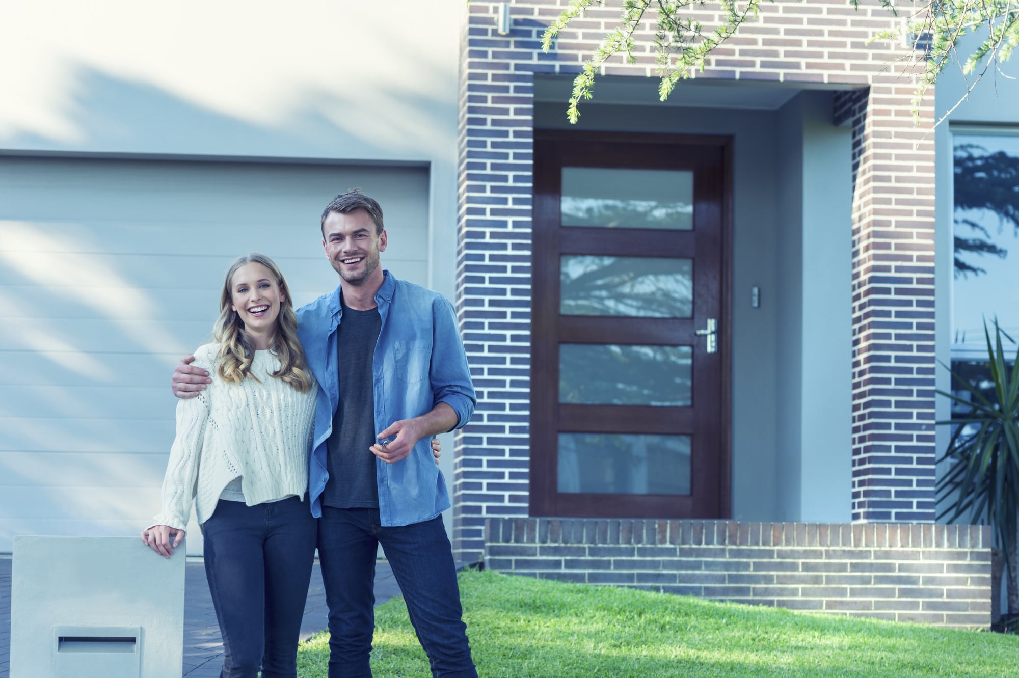 Young couple standing in front of their new home.
