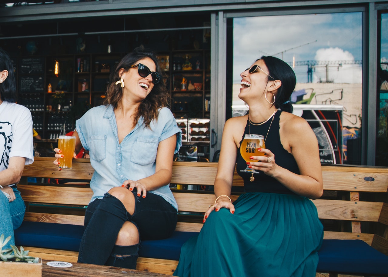 Two women laughing and holding glasses of beer.